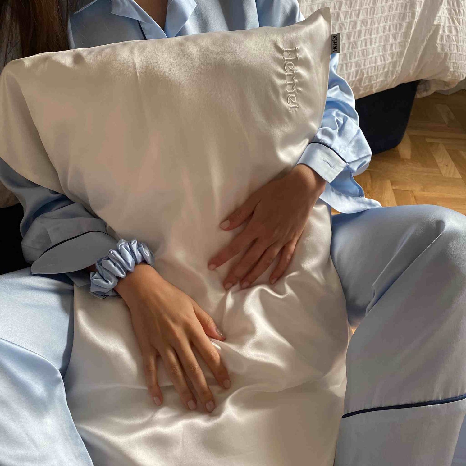 funda de almohada de seda de herriet en color blanca. La tiene una chica con el pijama de seda azul también de herriet