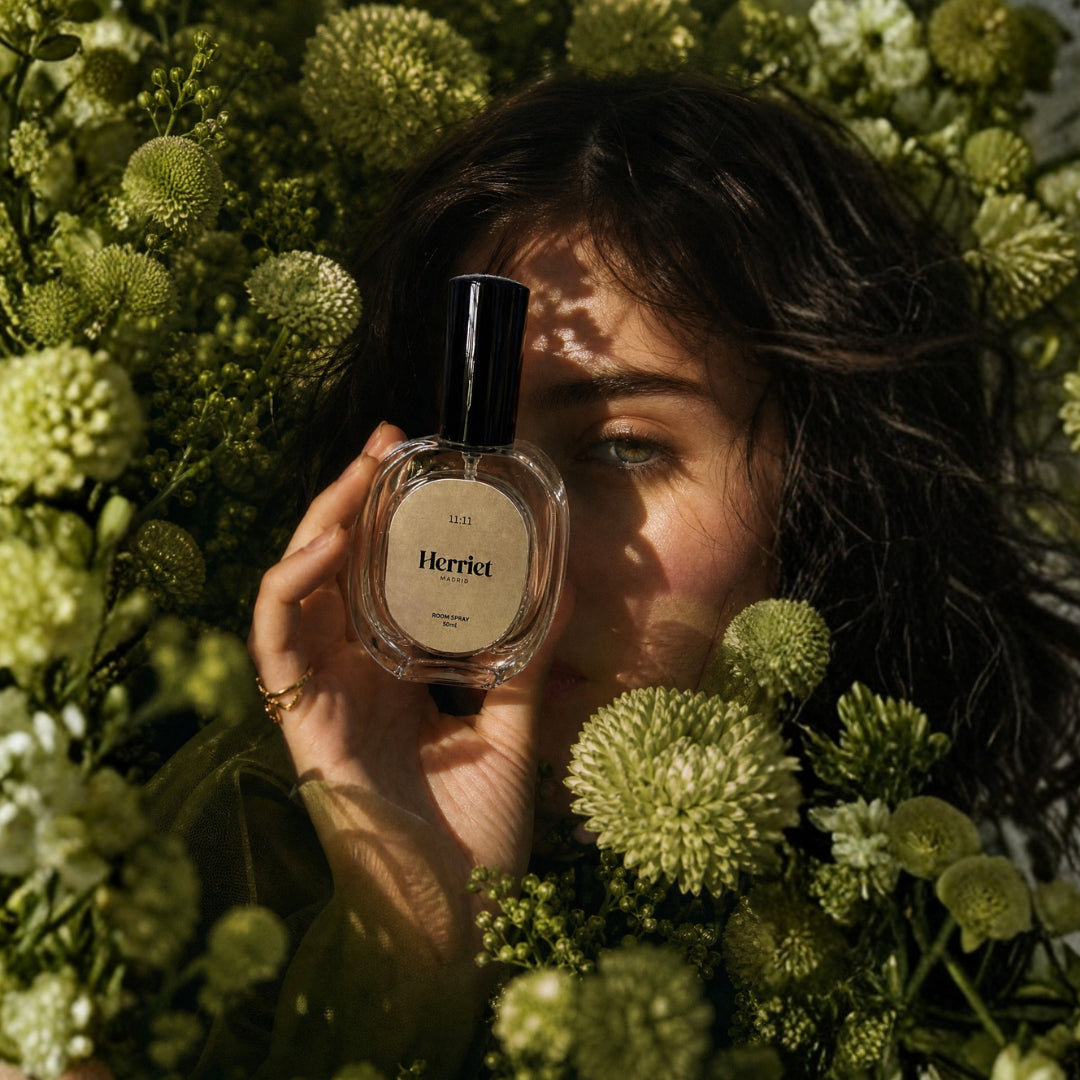 Person holding a Herriet room spray bottle among green flowers