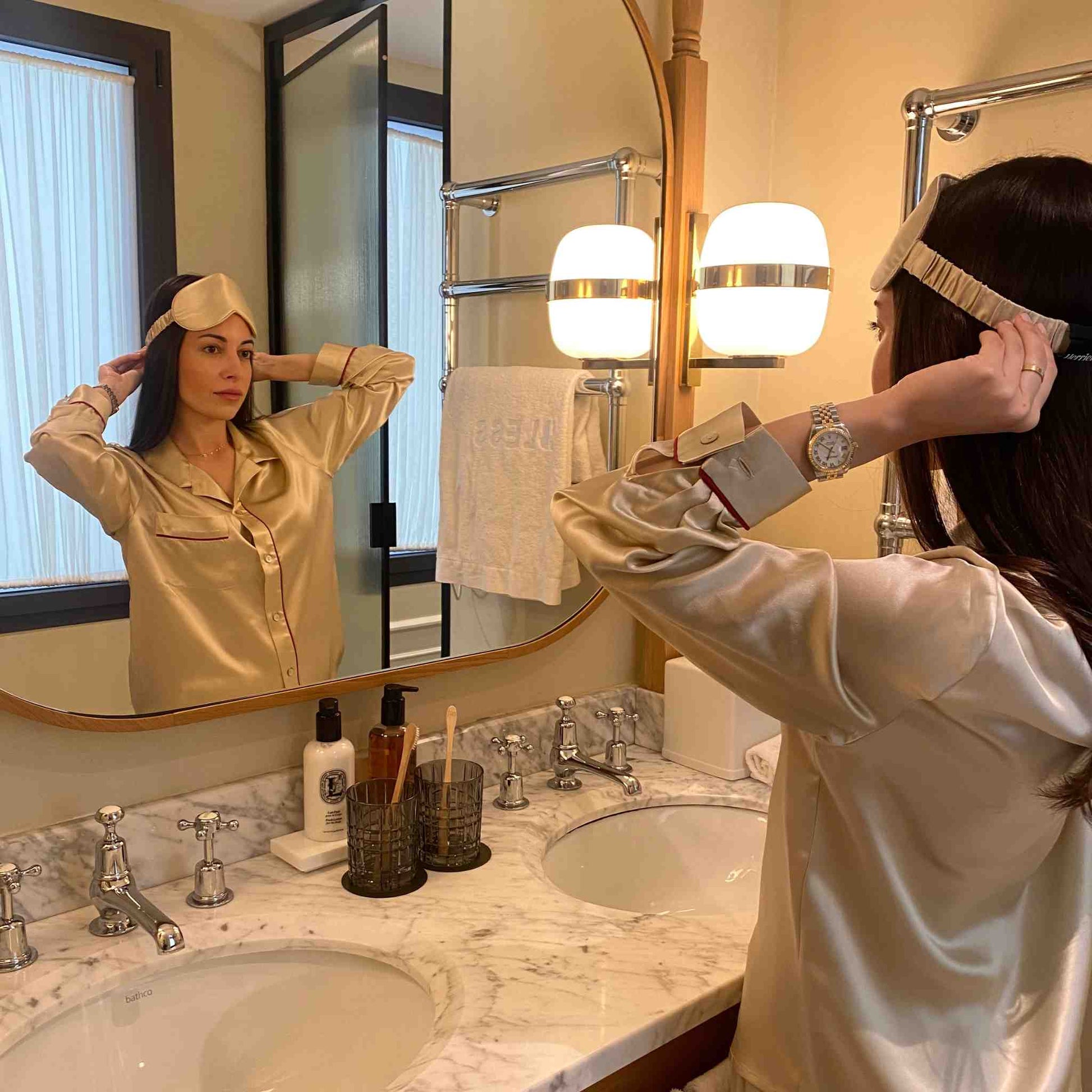 herriet - antifaz de seda para dormir en color beige. Chica mirandose al espejo con el antifaz puesto en la cabeza y el pijama de seda del mismo color de la marca