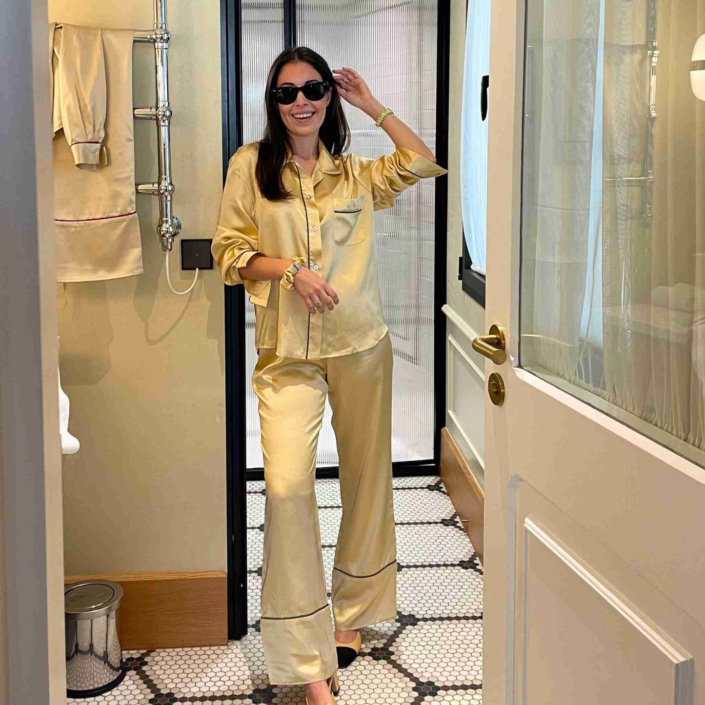 pijama de seda amarillo de herriet. Chica sonriendo y tocándose el pelo. Está en el baño del hotel bless y lleva tacones slingback de chanel